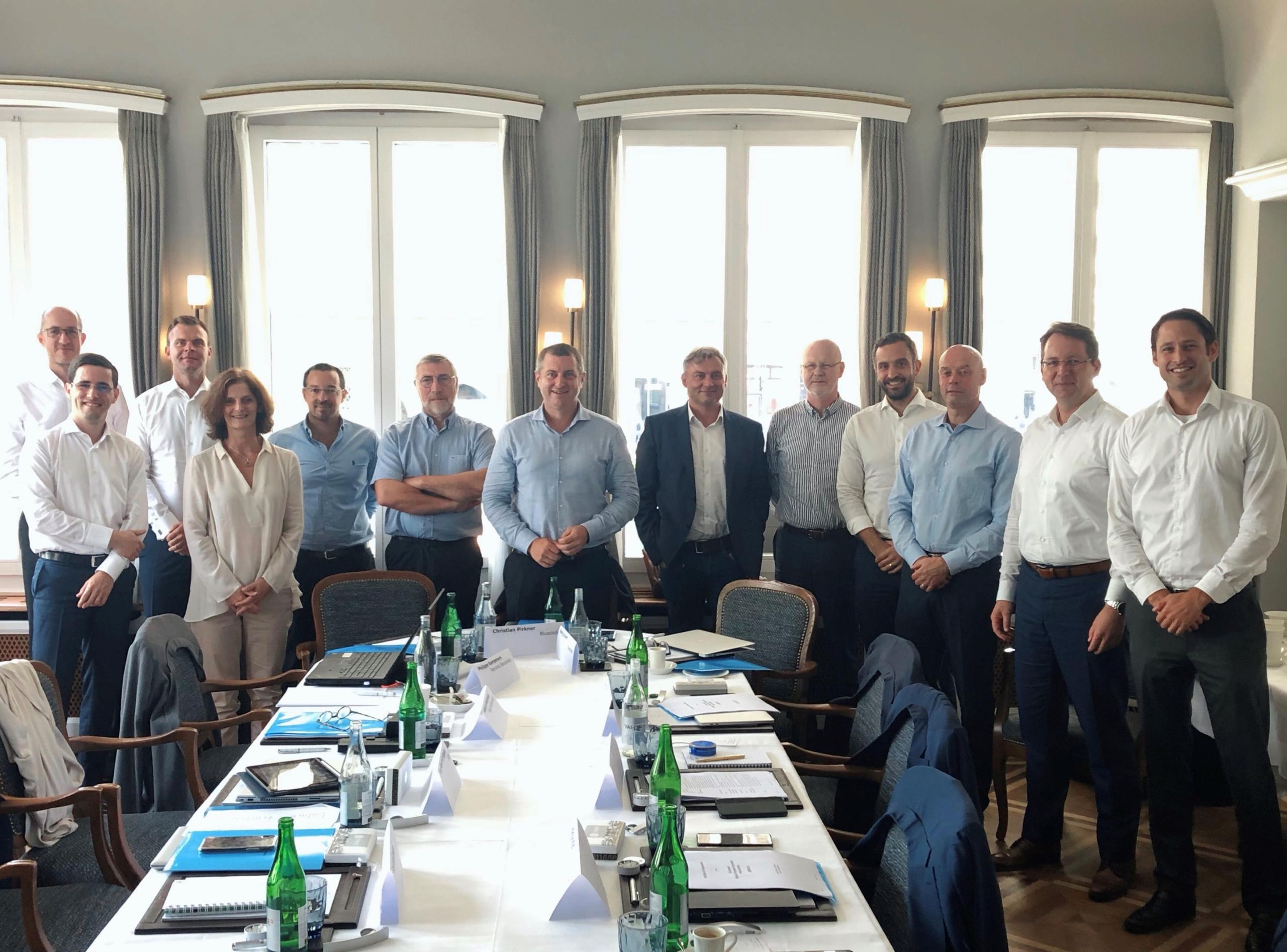 Gruppenfoto mehrerer Frauen und Männer hinter einem langen Tisch stehend, vermutlich Konferenzraum