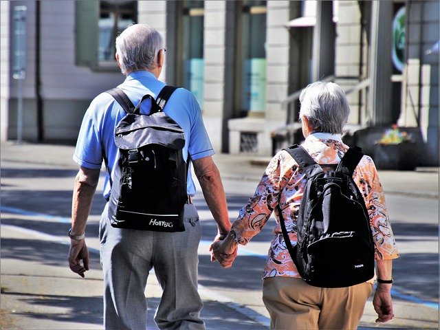 Ein älteres Paar spaziert mit Rucksächen durch eine Stadt