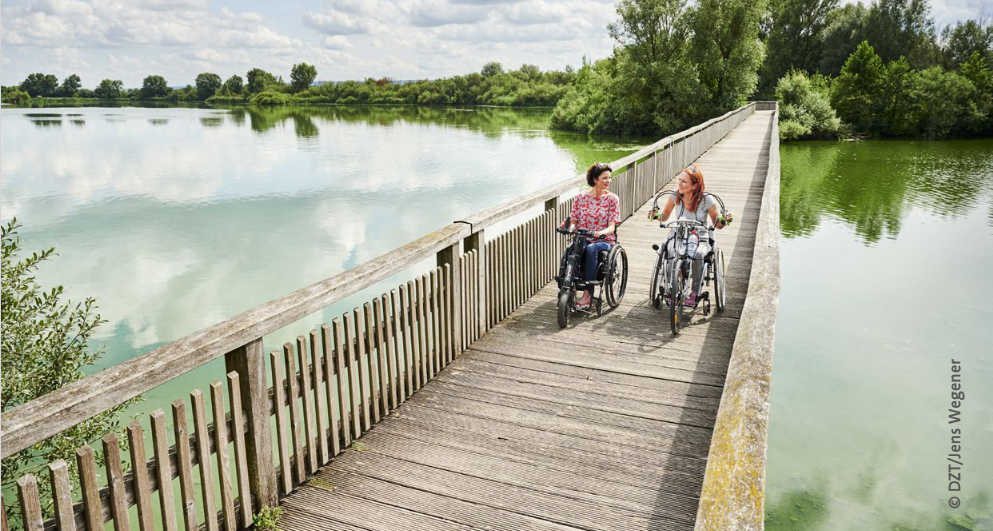 Zwei Frauen mit Handbikes fahren auf Holzbrücke