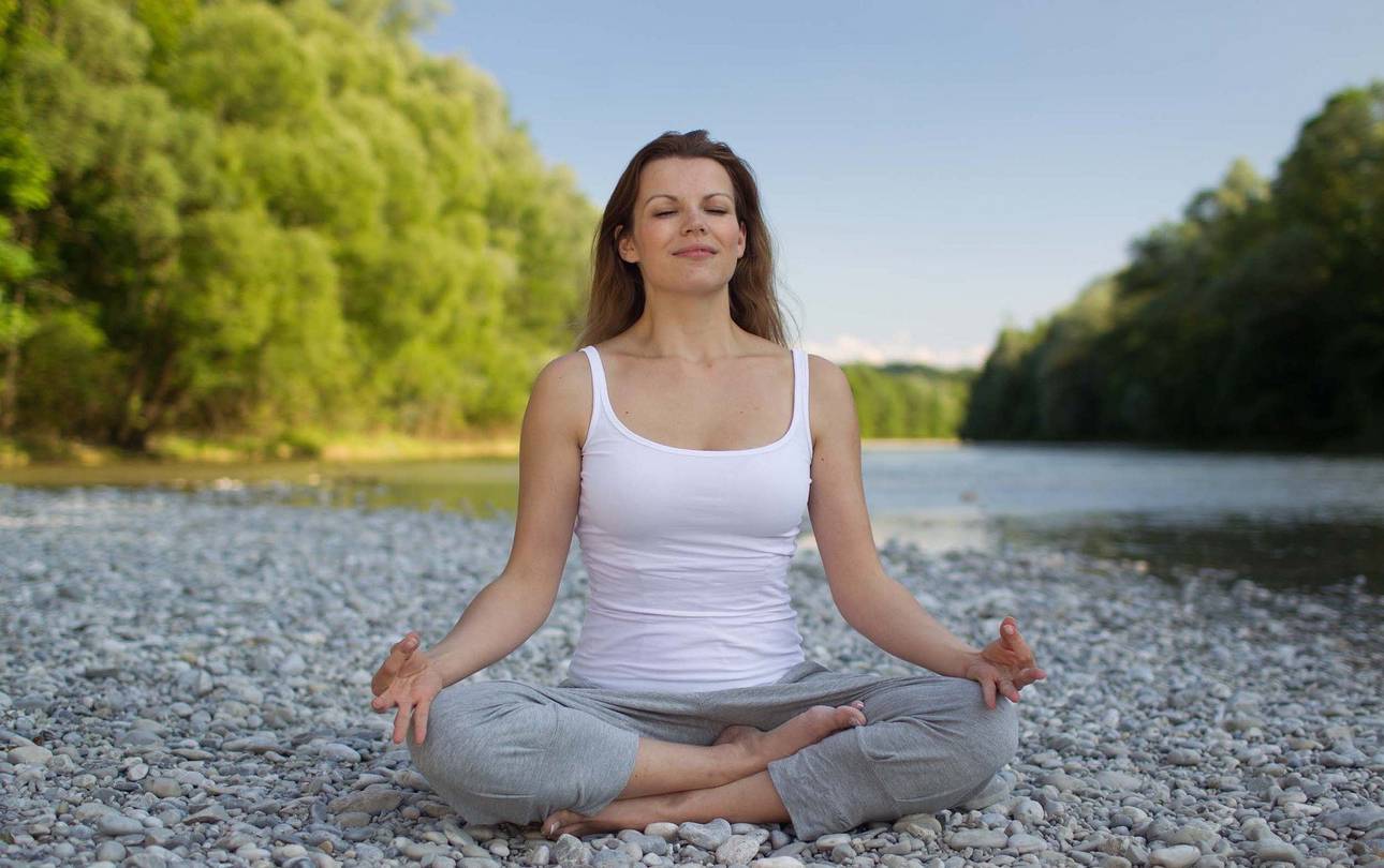 junge Frau meditiert im Schneidersitz am Flussufer