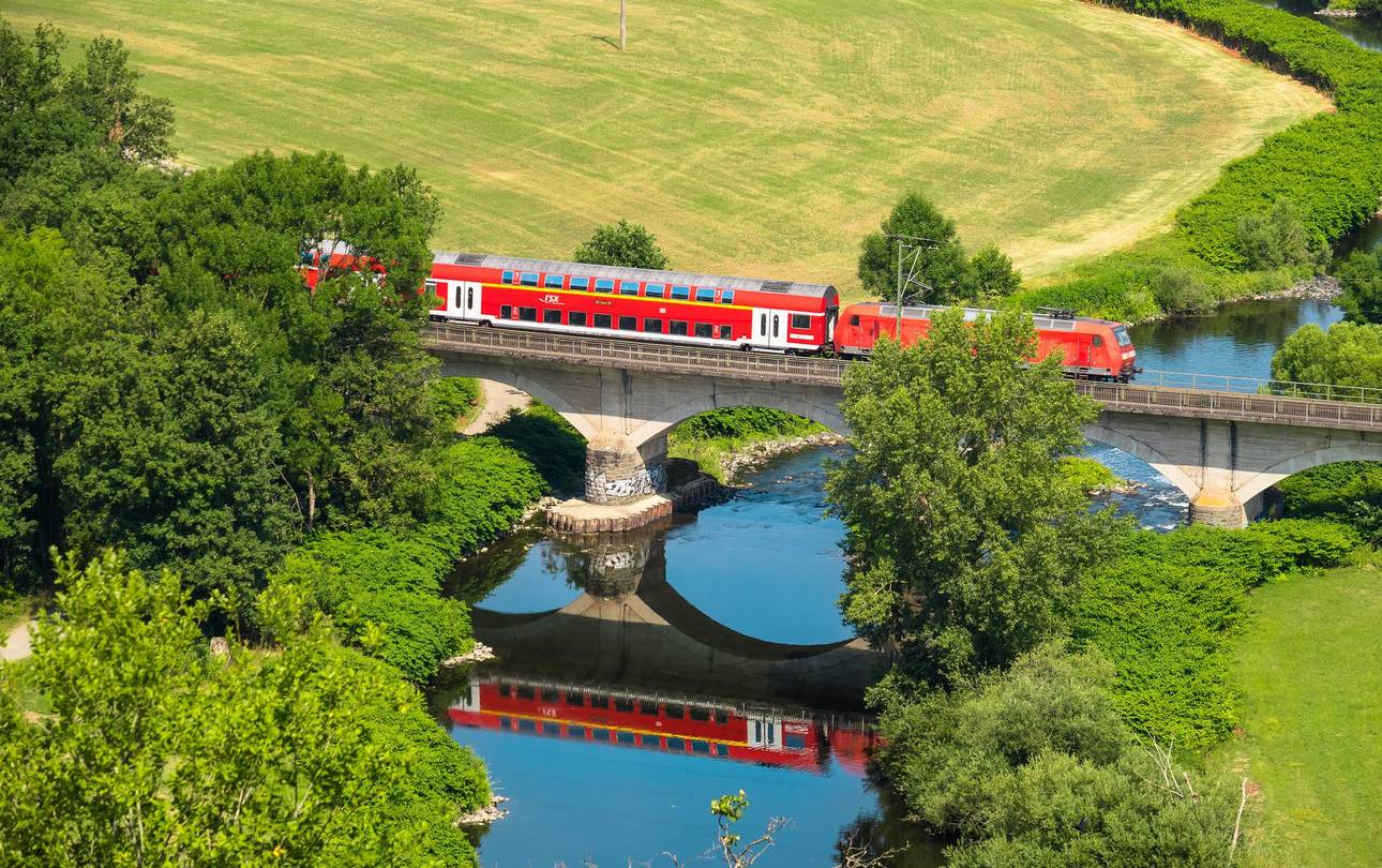 Regionalzug auf Brücke zwischen Wiesen und Feldern