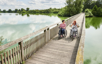 Zwei Frauen mit Handbikes fahren auf Holzbrücke