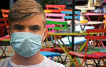 Junger Mann mit Maske vor leeren Restaurantstühlen