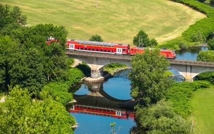 Regionalzug auf Brücke zwischen Wiesen und Feldern