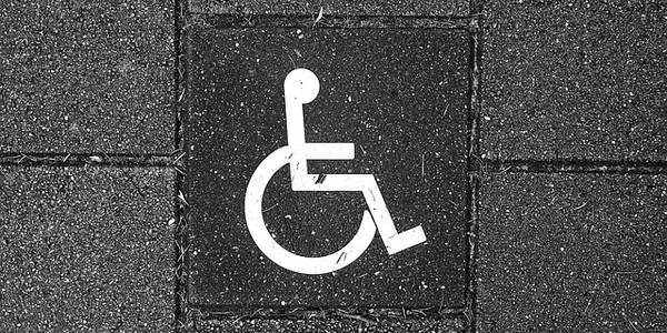 Ausschnitt eines Gewegs aus Betonsteinen mit weißem Rollstuhlpiktogramm