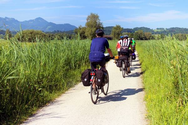 Radfahrer mit Fahrradtaschen auf Radweg zwischen grünen Feldern. Im Hintergrund Berge